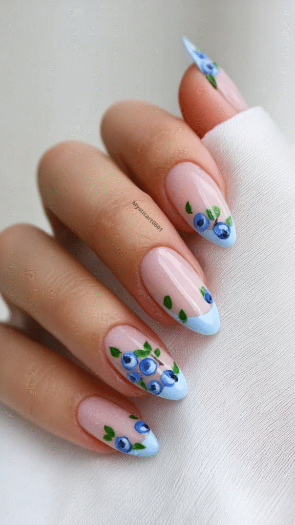 Cute blueberry nail art with hand-painted blue berries and green leaves on a nude base, pastel blue French tips – summer manicure idea